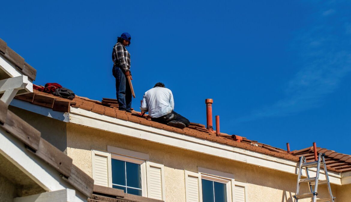 Two roofers working on a clay tile roof of a stucco home under a clear blue sky